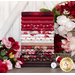 A stack of fabrics included in the Rory FQ Set in shades of brown, red, and white, displayed on a gray-brown table with coordinating flowers and thread for decor.