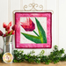Finished quilt block featuring a pink tulip with green leaves bordered by pink mottled fabrics laying on a wooden countertop and framed by greenery