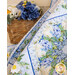 Photo of a blue, cream, and green floral quilt draped out of frame with a brown basket full of blue flowers in the background