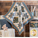a small blue and white quilt with sawtooth star shapes and square diamonds made with the Little Forest fabric collection hanging draped over a ladder against a brown paneled wall with a small shelf, blanket covered chair, and house plant in the background.