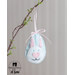 Close up of a pale blue easter egg ornament hanging by a pink ribbon on a branch with a white rabbit with pink ears and heart shaped nose.