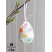 Close up of a white easter egg ornament hanging by a pink ribbon on a branch with small pastel flowers evenly spaced all over