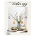 Six felt Easter egg ornaments hanging from an arrangement of spring buds on a table next to a bowl of colored eggs