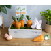 A white washed planter box filled with green moss and fabric carrots with a bunny figure diving into the box and a sign that says 