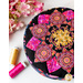 A round pink, yellow and black pincushion quilted in an intricate flower shape on a white marble countertop with pink and yellow spools of thread scattered nearby and pink flowers in the top left corner
