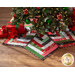 A festive tree skirt made with red, green, black, and white fabric strips under a decorated Christmas tree with wrapped gifts to one side.