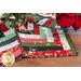 Close up of a festive tree skirt made with red, green, black, and white fabric strips under a decorated Christmas tree with Christmas decor of poinsettias in the top right of the photo