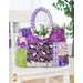 Finished tote bag made with purple and green floral fabrics filled with small purple and yellow flowers with green stems on a white chair in front of a white wall and houseplant in the background