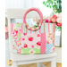 Finished tote bag made with pink, blue, and green floral fabrics filled with pink and white tulip flowers on a white chair in front of a white wall and houseplant in the background