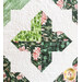 Close up of a single block showing a green cross shape on a white background, split into quadrants with differently patterned fabrics and swirling quilting detail