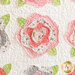 Close up of abstract rose design on a cream background showing layers of pink fabric and lightly frayed edges around petals and green leaf shapes.