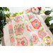Cream quilt with abstract roses made of layered fabric in shades pink draped over furniture with cream and pink flowers and green houseplants and a bright window in the background