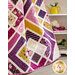 Image of geometric quilt gathered and draped in front of a white cabinet with a yellow teapot and stack of books.