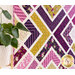 Close up angled photo of a geometric purple and yellow quilt hanging flat on a wall with a green houseplant in the foreground
