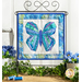 Photo of a blue and green butterfly made with foundation paper piecing techniques, hanging on a craft holder atop a counter with spring decor of flowers, foliage, and matching thread spools