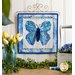 Photo of a blue and green butterfly made with foundation paper piecing techniques, hanging on a craft holder atop a counter with spring decor of flowers, foliage, and matching thread spools