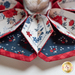 Close up of a flower shaped table topper with central opening with a small jar and patriotic decor in the background. Topper is made of crisp white, red and navy blue fabrics with multicolor florals.
