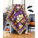 A Halloween-themed quilt draped over a ladder in front of a white paneled wall with Halloween decor on a white shelf and small black chair