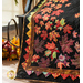 Close up photo of the Autumn Allure quilt showing applique leaf details and a decorative basket with fall decor in the background