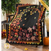 Photo of the Autumn Allure quilt made with black, purple, red, green, orange, and brown metallic fabrics draped over a chair with tall houseplants and fall decor in the background