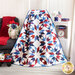 Photo of a large patriotic quilt draped in front of a dark grey arm chair and small white shelf with a small red wagon and patriotic decor and flowers in front of a white paneled wall