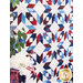 an angled photo of a geometric patriotic-themed quilt hung vertically against a wall with a white flower and green houseplant in the foreground
