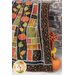 Large autumn themed quilt draped over furniture in front of a stone wall with a pumpkin and small stool with flowers on the floor.
