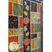 Angled photo of large, autumn themed quilt in green, orange, black, and yellow with pumpkin and oak leaf applique details hanging on a wall