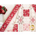 Close up photo of a red, pink, and cream quilt made with traditional style quilt star blocks and diamond blocks draped against a white paneled wall with a white shelf and red roses.