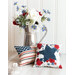 A white paneled wall and white countertop with two patriotic pillows in the foreground and a metal pitcher full of flowers behind them