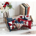 A white countertop and white paneled wall with a collection of small patriotic themed pillows in a wire basket in the foreground with three books and a metal pitcher filled with flowers in the background.