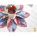 Leaf shaped table topper with central opening containing a floral centerpiece. Topper is made of red white and blue patriotic fabrics.