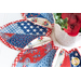 Close up of leaf shaped table topper with central opening containing a floral centerpiece. Topper is made of red white and blue patriotic fabrics.