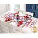 Photo of a patriotic red white and blue table runner in a patchwork pattern on a white table with four place settings, each with matching red napkins in rings, a patriotic centerpiece with a small American flag, and a bright window in a blue wall in the background
