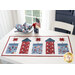 a patriotic table runner with five quilted fireworks on a white background, on a white table next to a stack of plates and matching napkins, and a small bucket with flowers and an American flag in it with a white chair and a window in the background