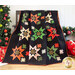 Photo of Merry & Bright Quilt draped over a chair or bench in front of a white paneled wall with Christmas decor in the background.