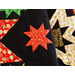 Close up of Merry & Bright Quilt showing a small starburst design made with black, red, green, and cream fabrics with Christmas motifs and metallic accents