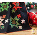 Close up of Merry & Bright Quilt draped in front of a decorated Christmas wreath with a small red sleigh filled with wrapped gifts in the middleground