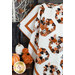 Close up photo of a quilt featuring rows of blocks with patchwork pumpkins made with orange, cream, and black fabrics. Quilt is draped in the foreground with Halloween decor in the background