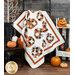 A photo of a pumpkin and Halloween themed quilt draped in front of a gray paneled wall with halloween decor all around