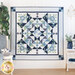 Photo of finished geometric and floral quilt hanging flat on a white paneled wall with white furniture and blue nautical decor items with a green houseplant on the sides.