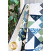 Close up of draped geometric and floral quilt made with navy, light blue, cream and green fabrics with a green houseplant in the background