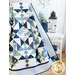 Angled photo of draped geometric and floral quilt made with navy, light blue, cream and green fabrics with a white wicker table and nautical decor in the background