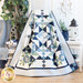 Photo of draped geometric and floral quilt made with navy, light blue, cream and green fabrics with a white wicker table and nautical decor on one side and a chair, blue blanket and green houseplant in the background on the left.