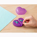 A hand placing a heart shaped sewing pin on a purple heart shaped magnetic pin caddy