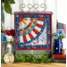 Photo of finished patriotic quilt square on a craft hanger sitting on a brown countertop with a white paneled wall in the background and patriotic decor and plants on either side.