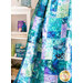 Close up of a draped blue, green, and purple quilt with a white shelf and matching decor in the background.