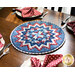 Image of a red, white, and blue circular table topper with a miniature quilt block center piece. The table topper is set on a brown wood table with spotted cloth napkins atop four white plates with place settings all around it