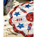 A red, white, and blue scalloped table topper with fireworks and stars sitting on a table next to golden scissors