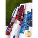 Gathered red white and blue quilt on a white wicker chair with green grass in the background